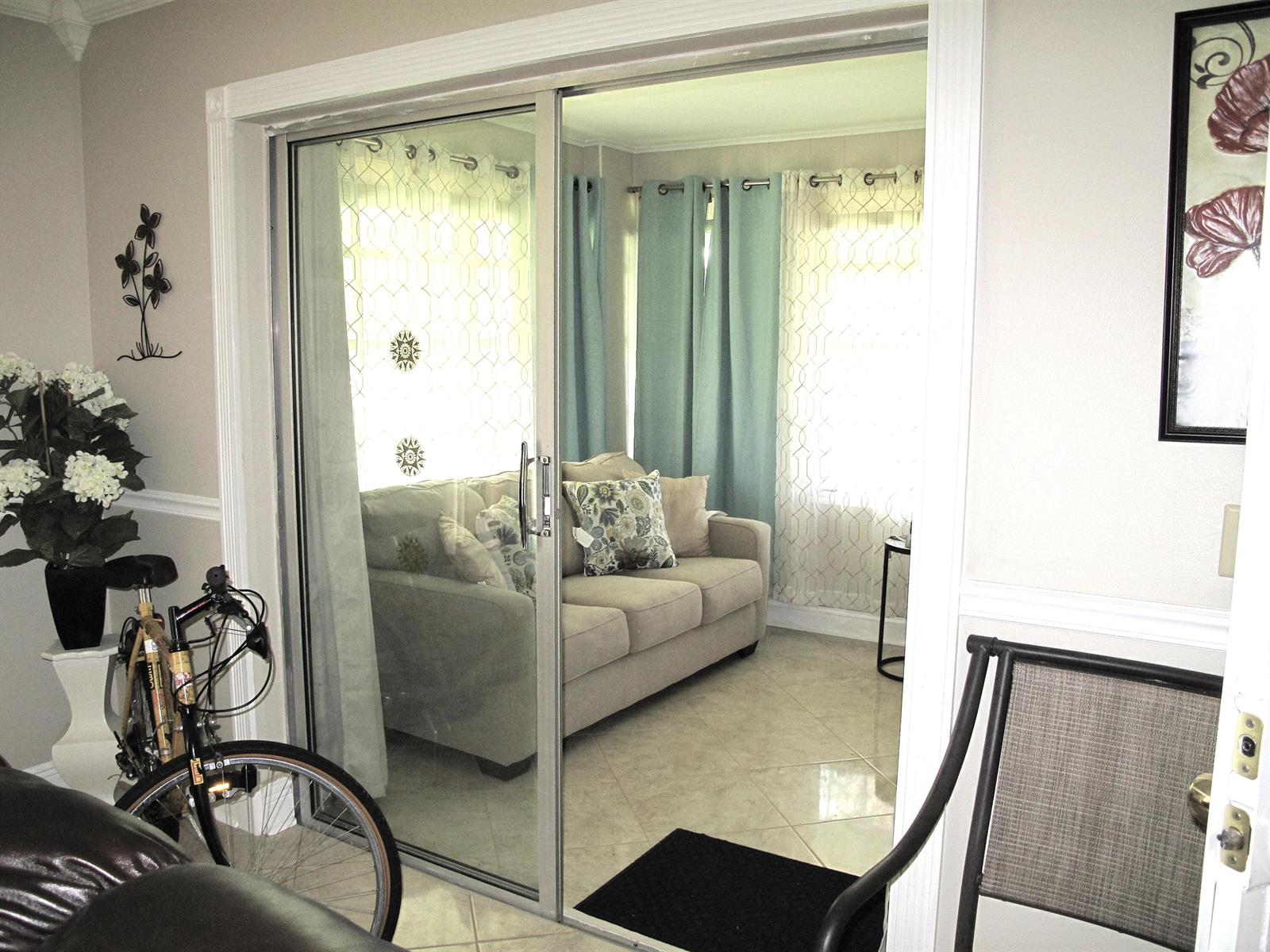 A sliding glass door opens into a sunroom featuring a sofa, tile floors, and curtains — 892 N High Point Boulevard N # D, Delray Beach FL 33445, DELRAY BEACH, FL