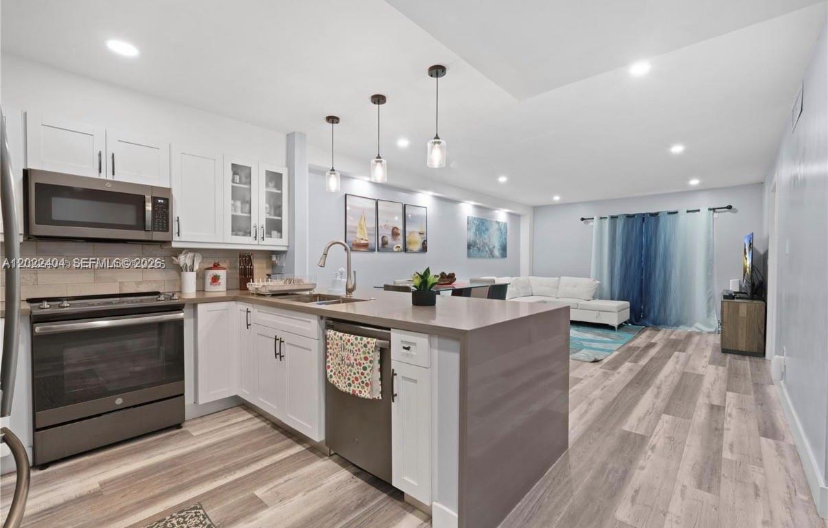 A modern kitchen with white cabinets and a gray island opens into a living area — 6125 W 20th Ave # 302, Hialeah FL 33012, HIALEAH, FL