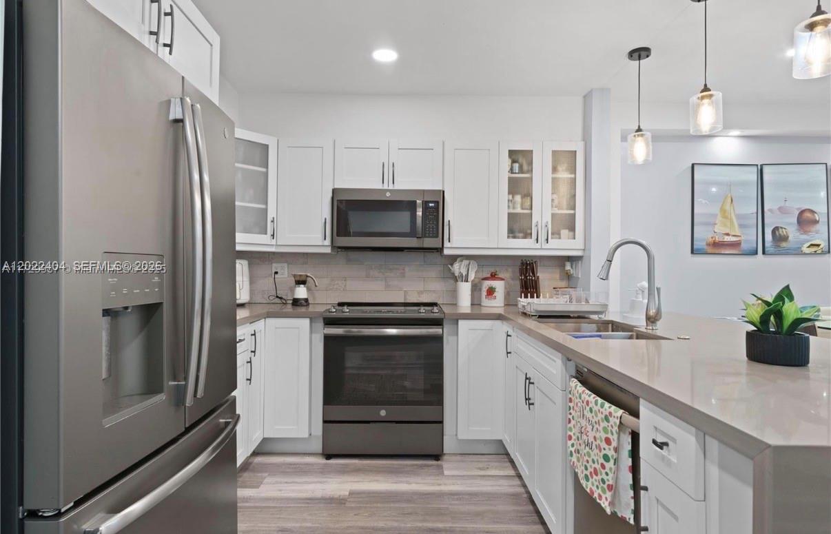 A modern kitchen features white cabinets, stainless steel appliances, and a quartz countertop island — 6125 W 20th Ave # 302, Hialeah FL 33012, HIALEAH, FL