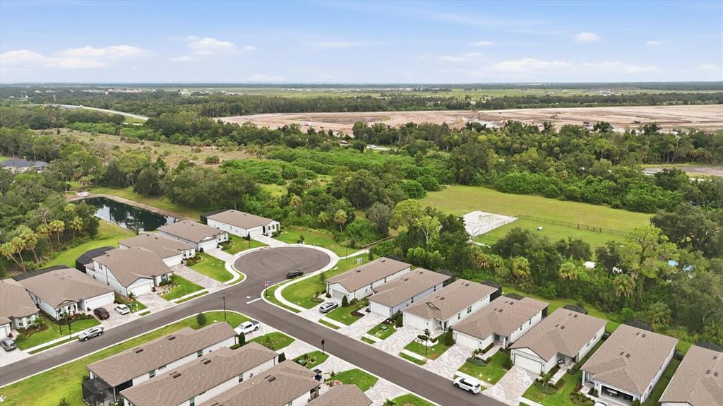 An aerial view shows a suburban neighborhood with rows of houses, a pond, and undeveloped land — 9410 SHOREBIRD COURT, PARRISH, FL