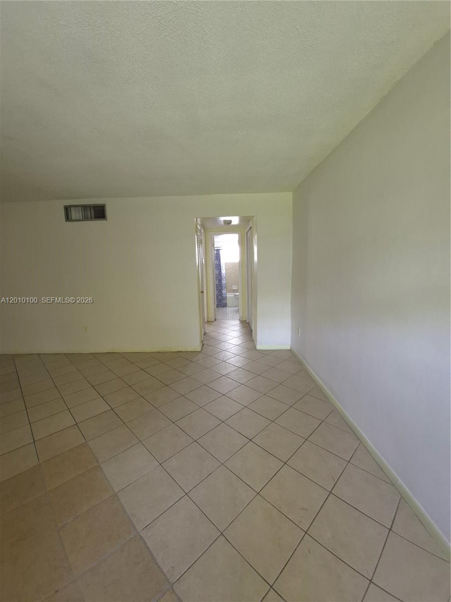 A room with beige tile flooring leads through a doorway into a hallway — 1826 Cleveland St # 3, Hollywood FL 33020, HOLLYWOOD, FL