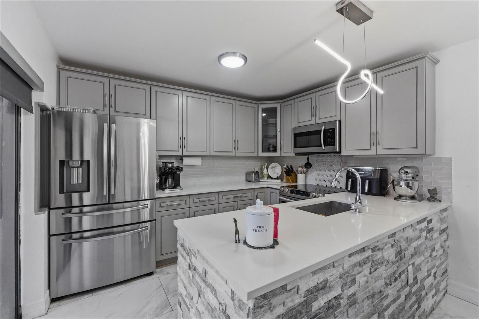 A kitchen features gray cabinets, stainless steel appliances, a stone-faced island, and white countertops — 1017 10th Way, West Palm Beach FL 33407, WEST PALM BEACH, FL