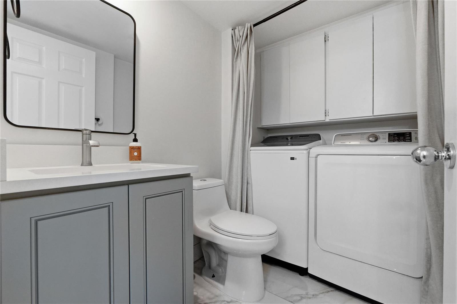 A bathroom featuring a gray vanity, a toilet, and a laundry area with white appliances — 1017 10th Way, West Palm Beach FL 33407, WEST PALM BEACH, FL