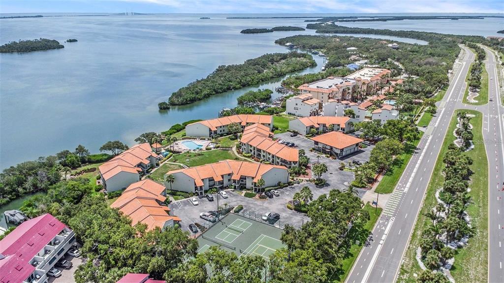 An aerial view shows a waterfront residential complex with a pool, tennis courts, and parking — 1515 PINELLAS BAYWAY S UNIT 26, ST PETERSBURG, FL