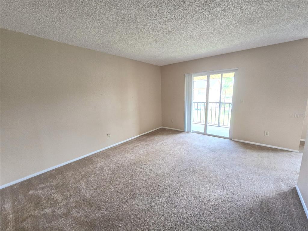 An empty living room features beige carpet, tan walls, and a sliding glass balcony door — 9933 SWEEPSTAKES LANE UNIT 4, ORLANDO, FL
