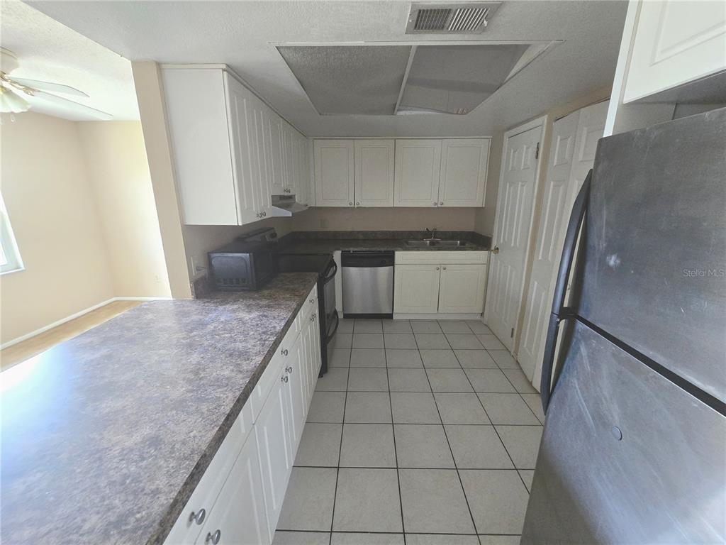 A kitchen features white cabinets, dark countertops, stainless steel appliances, and light-colored floor tiles — 9933 SWEEPSTAKES LANE UNIT 4, ORLANDO, FL