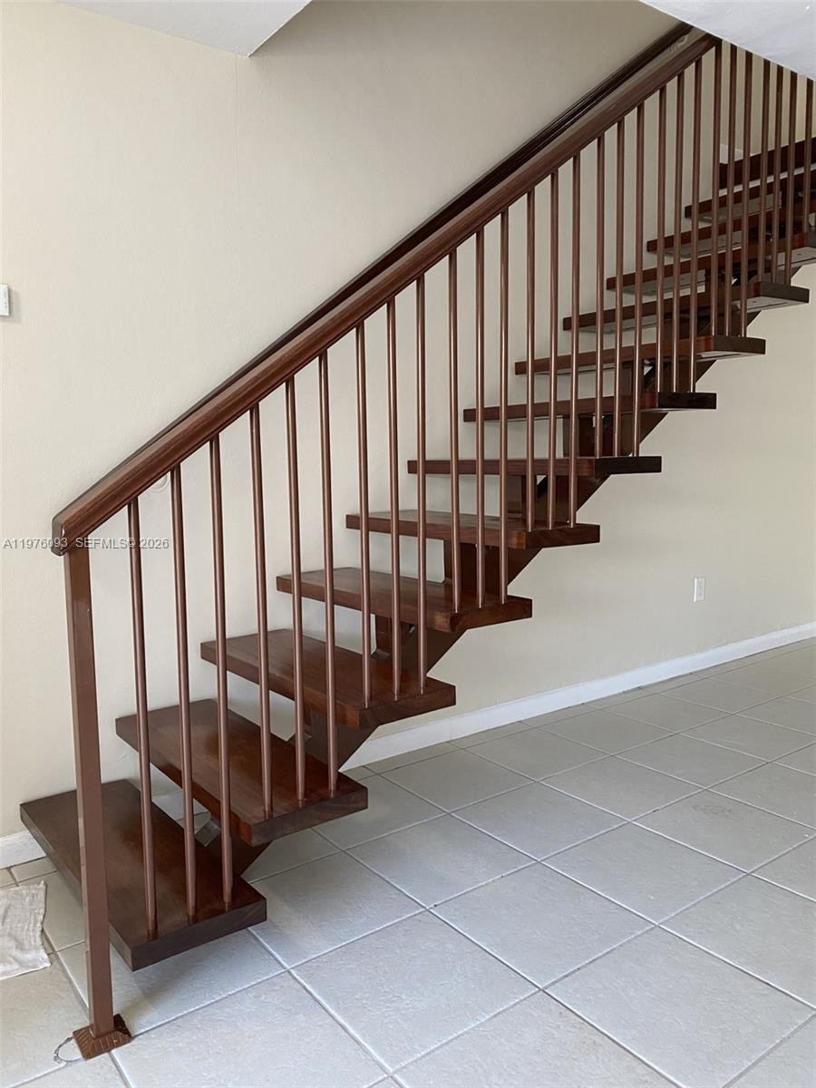 A wooden staircase with open risers and a matching railing stands against a beige wall — 2183 NE 122nd St # 2183, North Miami FL 33181, NORTH MIAMI, FL