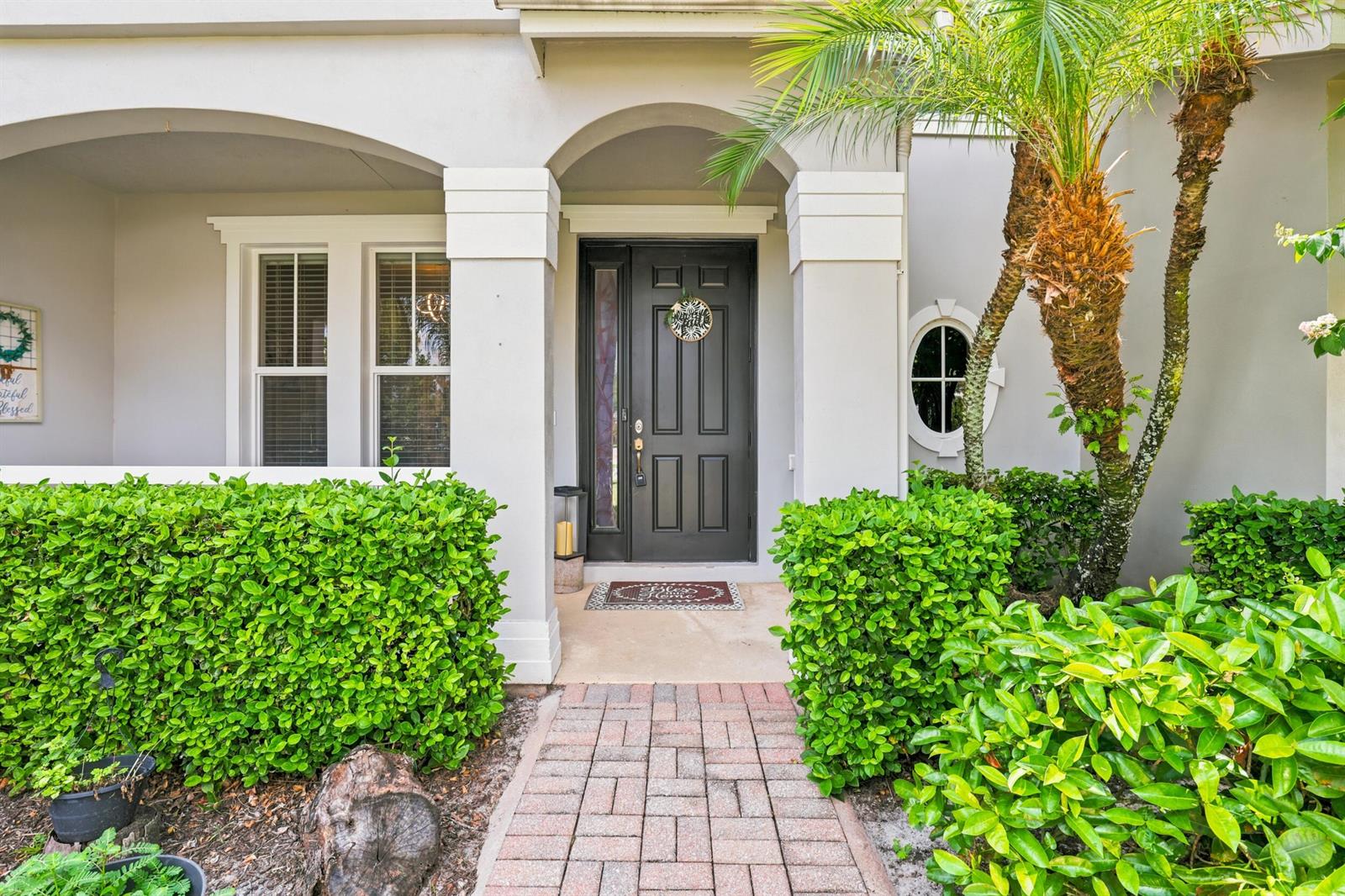 A front entryway features a dark door, brick walkway, and manicured hedges under an archway — 10487 SW West Park Avenue, FL 34987, FL
