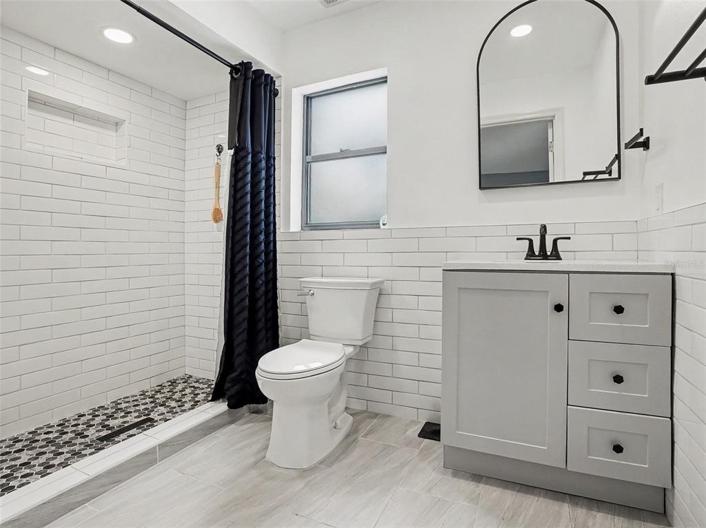 A bathroom features a walk-in shower, a toilet, and a gray vanity with subway tile — 1006 WHEELER PLACE, OVIEDO, FL