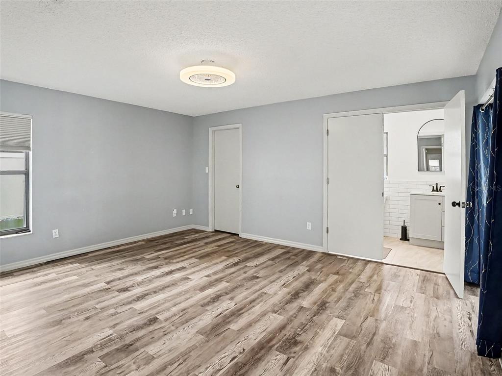 A bedroom with light gray walls, wood-look flooring, a ceiling light, and an attached bathroom — 1006 WHEELER PLACE, OVIEDO, FL