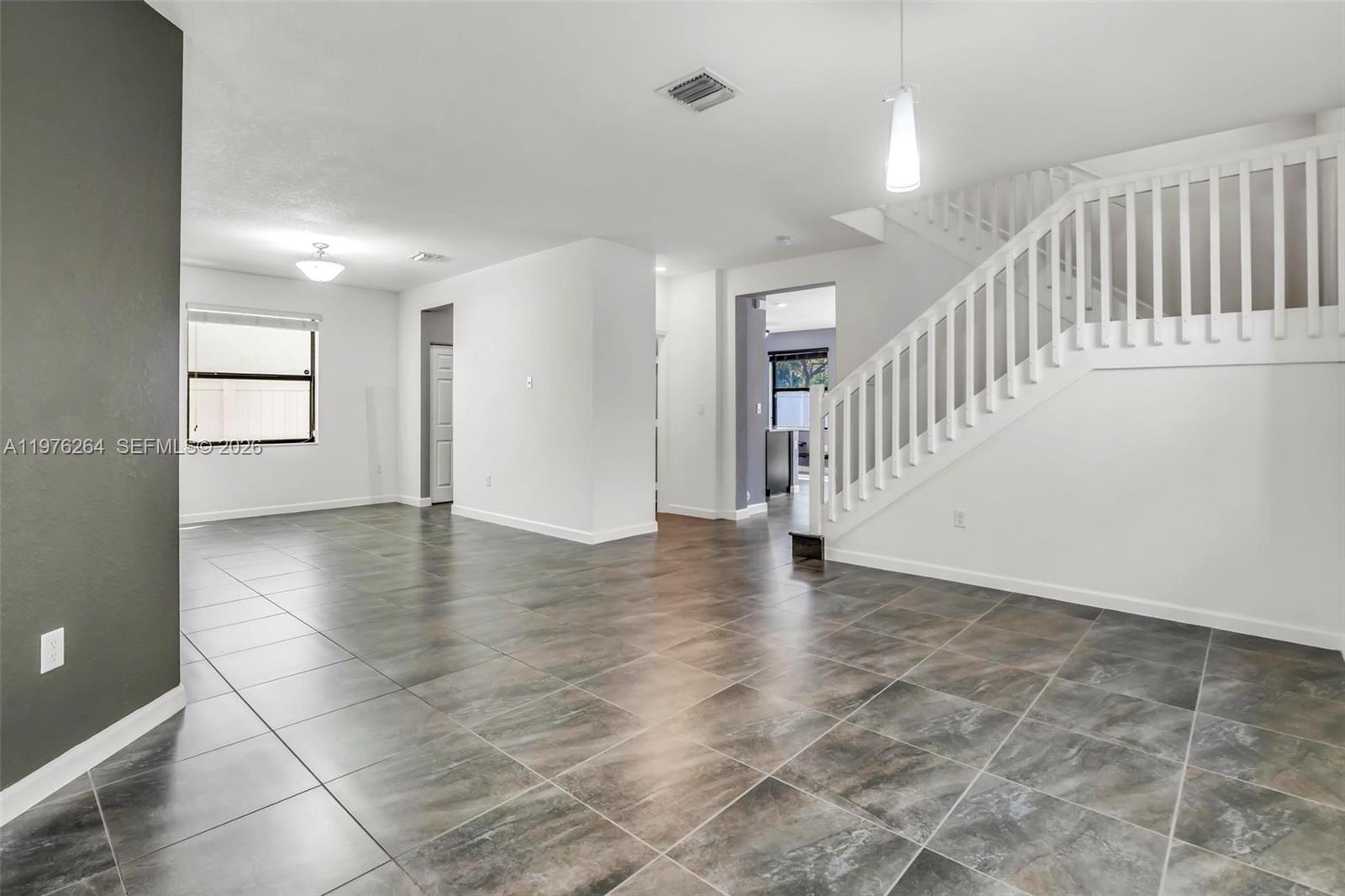 An open living area features large gray floor tiles, white walls, and a wooden staircase — 3440 W 100th Ter, Hialeah FL 33018, HIALEAH, FL