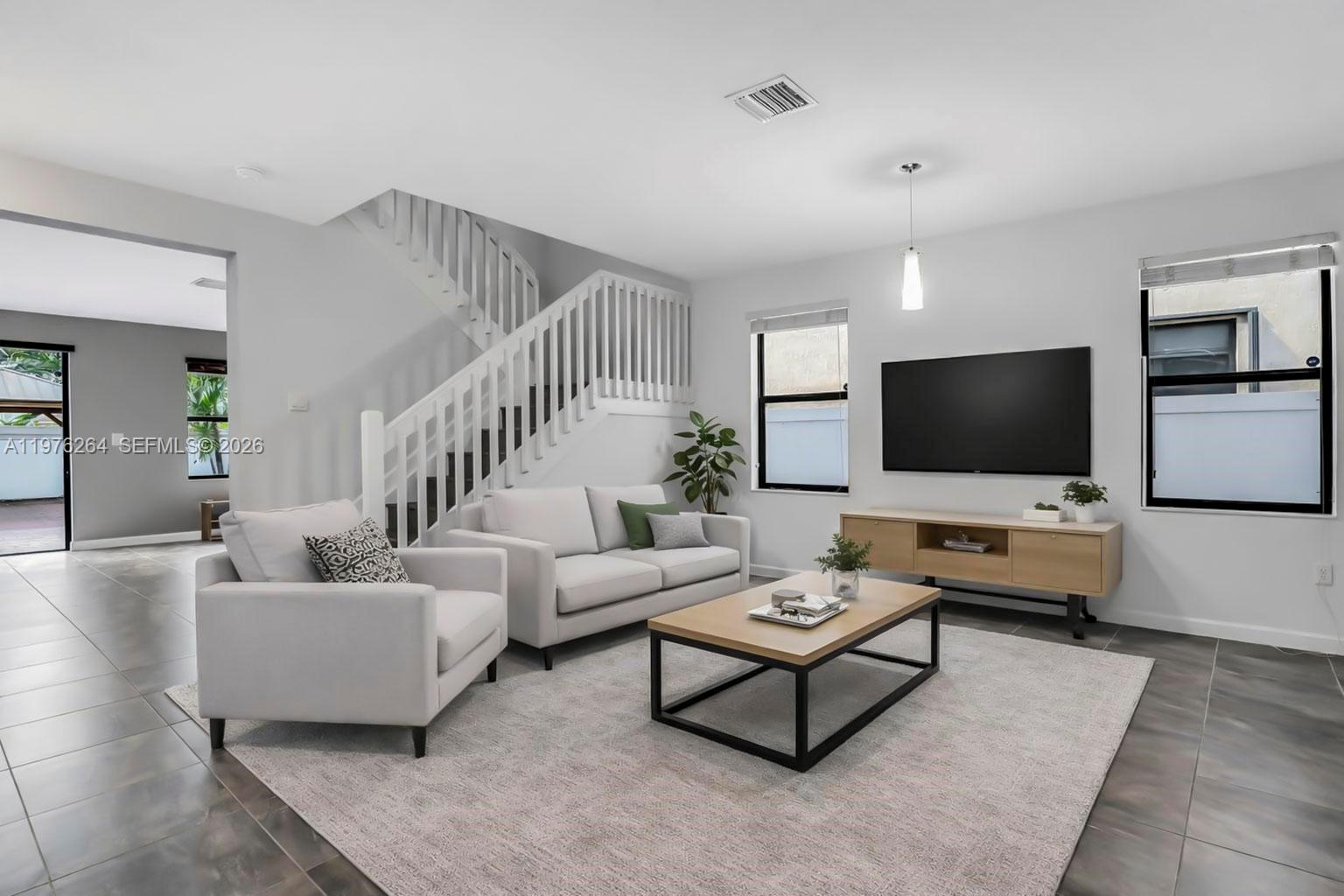A modern living room features a white sofa, armchair, coffee table, and a staircase — 3440 W 100th Ter, Hialeah FL 33018, HIALEAH, FL