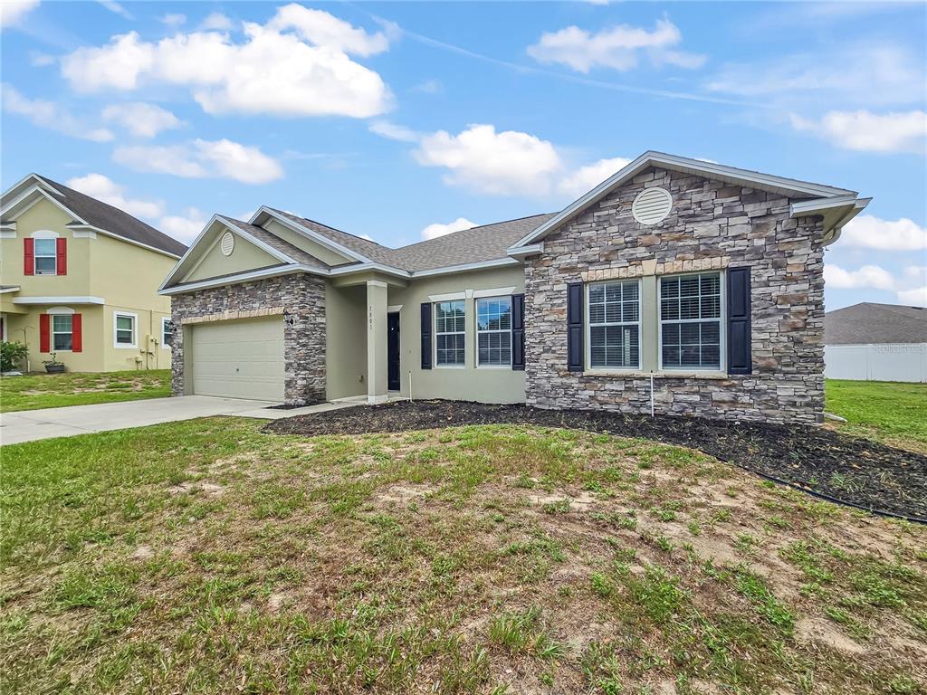 A single-story house features a stone facade, a two-car garage, and a patchy grass lawn — 1801 HOOFPRINT COURT, FRUITLAND PARK, FL