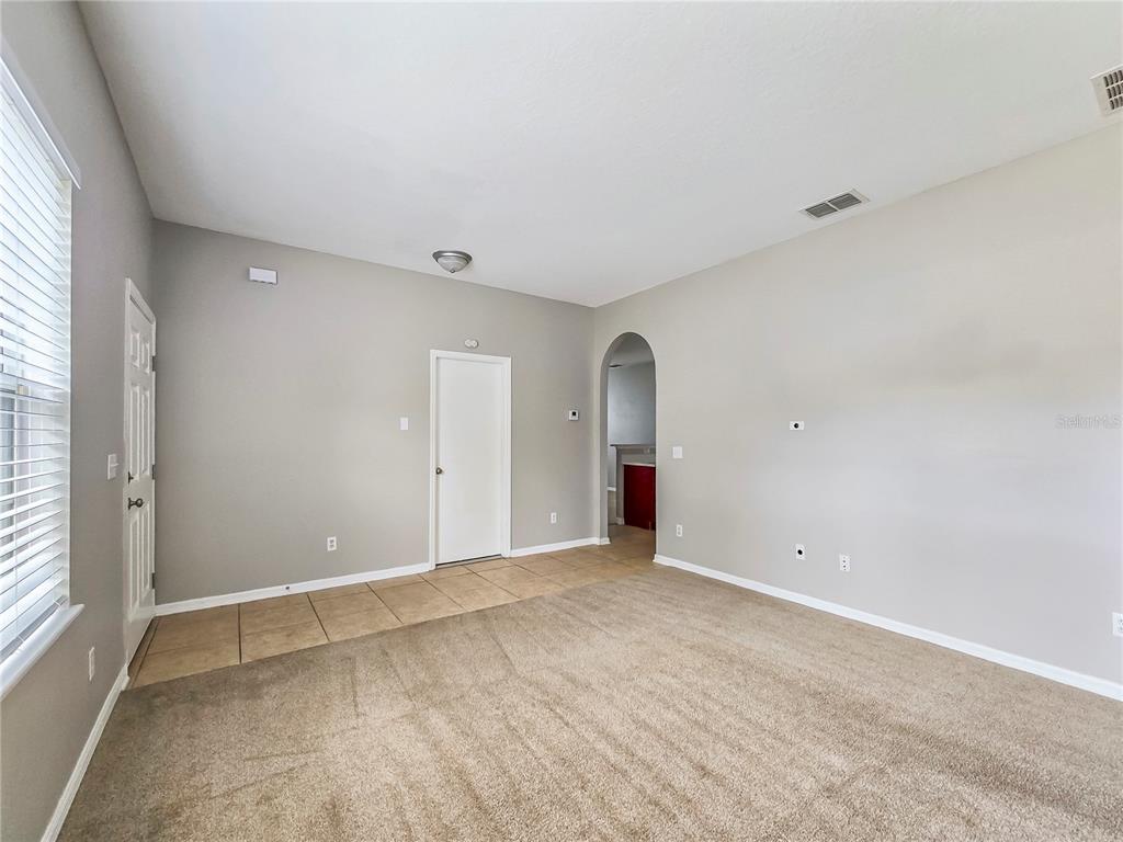 A room with beige carpet, tiled entryway, light gray walls, and an arched doorway — 1801 HOOFPRINT COURT, FRUITLAND PARK, FL
