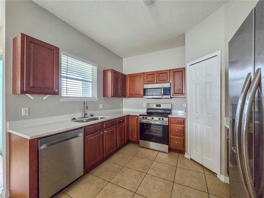 A kitchen features wood cabinets, stainless steel appliances, white countertops, and tiled flooring — 1801 HOOFPRINT COURT, FRUITLAND PARK, FL