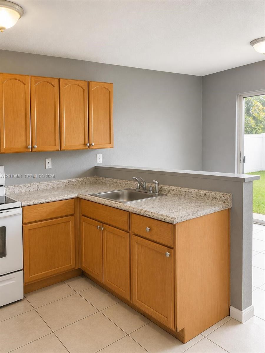 A kitchen features oak cabinets, speckled laminate countertops, a stainless steel sink, and tile flooring — 8180 NW 23rd Ave # A, Miami FL 33147, MIAMI, FL
