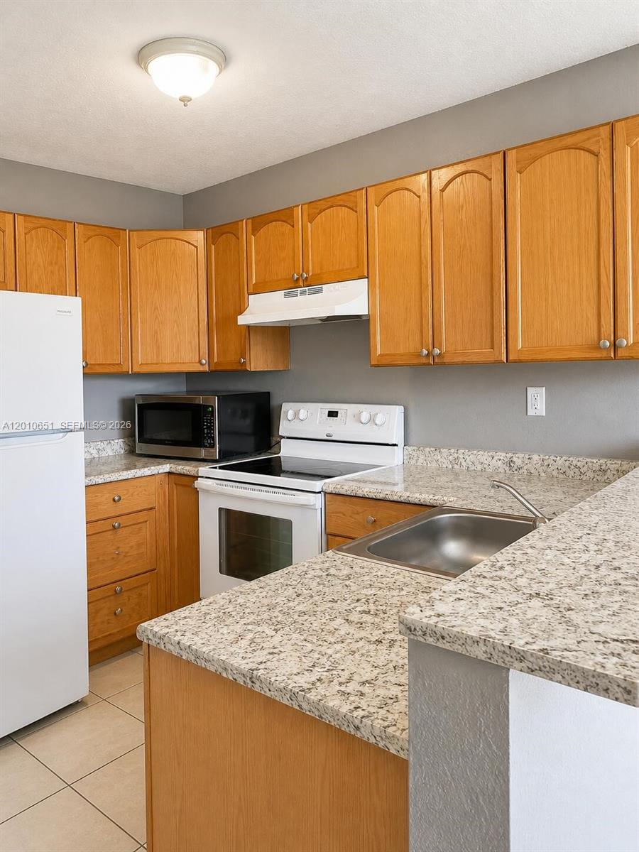 A kitchen features oak cabinets, granite countertops, a white refrigerator, and a stainless steel sink — 8180 NW 23rd Ave # A, Miami FL 33147, MIAMI, FL