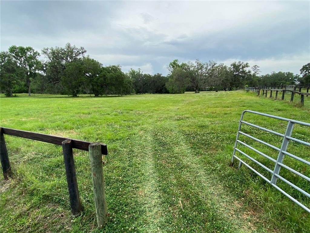 A grassy pasture is enclosed by a metal gate and wooden fence under a cloudy sky — 0 N HWY US 27, OCALA, FL