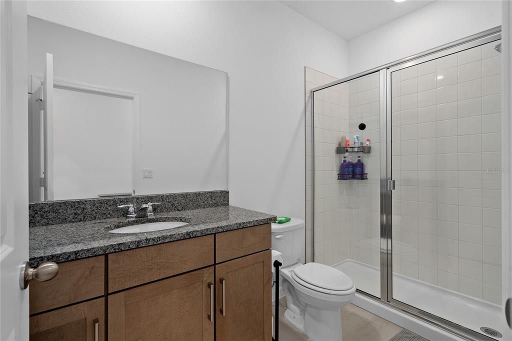 A bathroom features a granite-topped vanity, a white toilet, and a glass-enclosed tiled shower — 655 CLARK STREET, OVIEDO, FL
