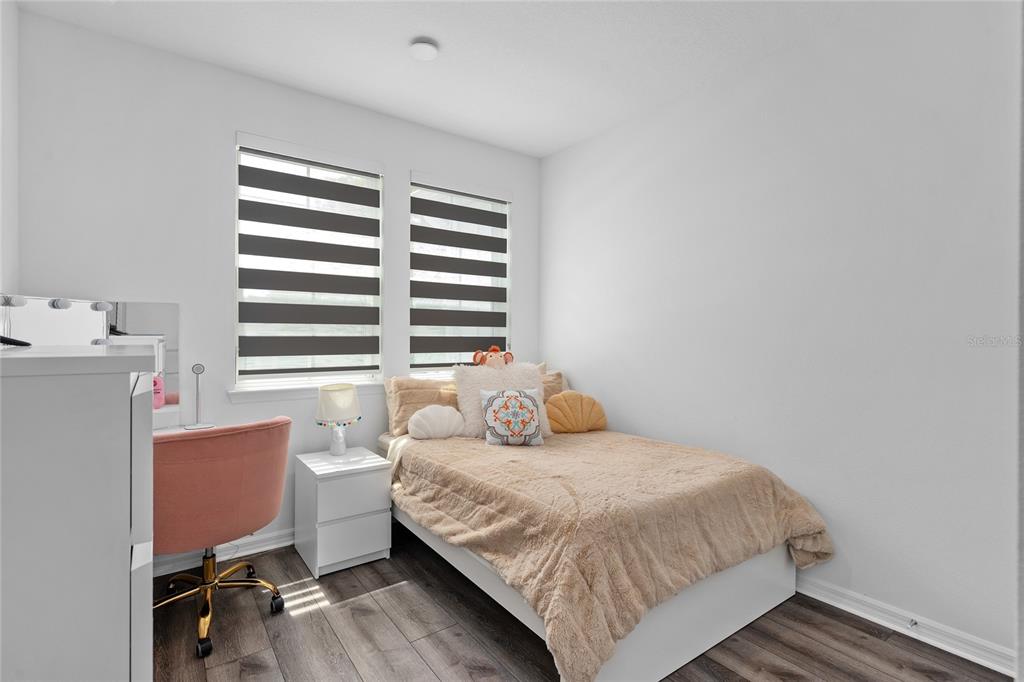 A bedroom features a bed with tan bedding, a white nightstand, and a pink chair — 655 CLARK STREET, OVIEDO, FL