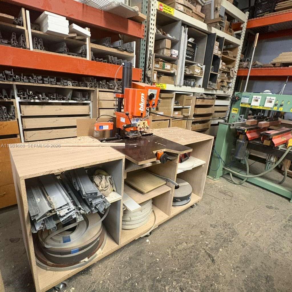 A workshop features a Blum hinge boring machine on a wooden workbench with storage shelving — 2683 76, Hialeah FL 33016, HIALEAH, FL