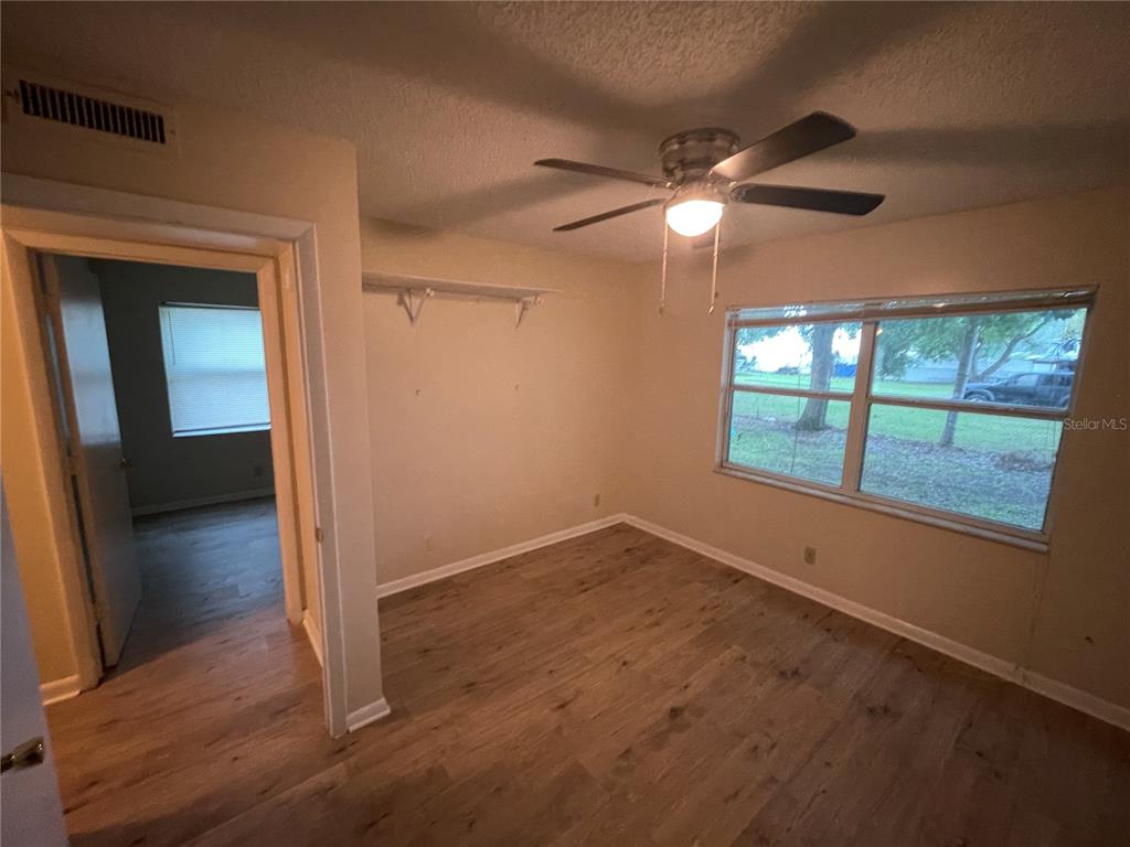 An empty bedroom with wood-look flooring, a ceiling fan, and a window overlooking a yard — 230 MILLARD AVENUE UNIT 1, LAKELAND, FL