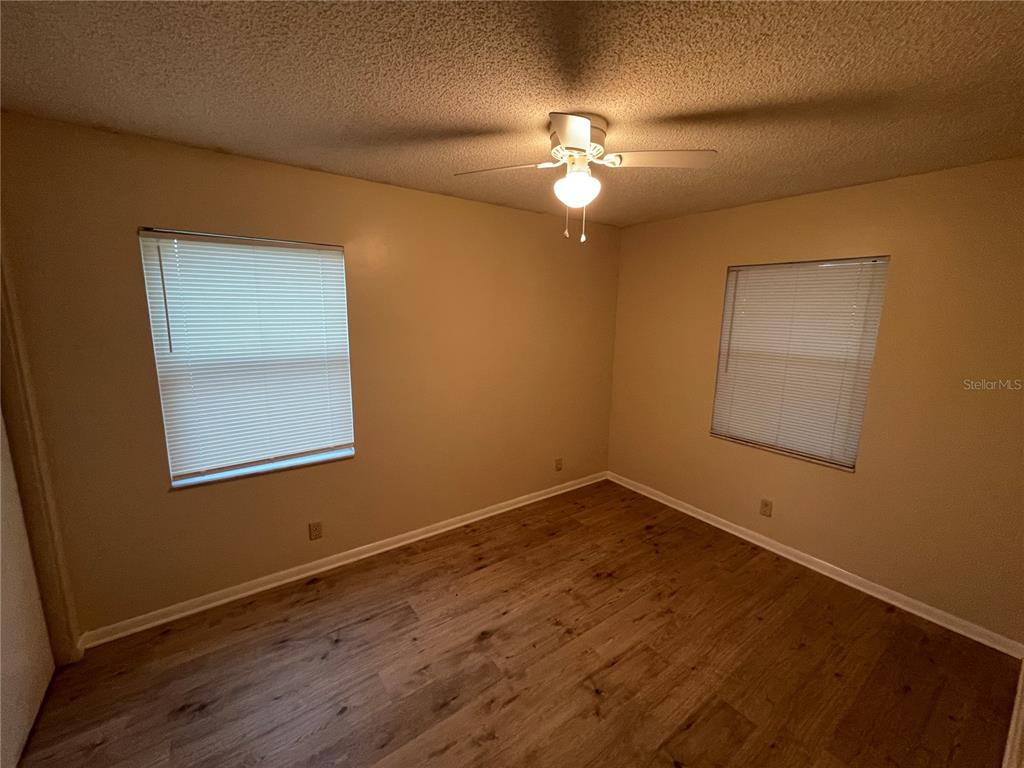An empty bedroom features light-colored walls, wood-look flooring, two windows with blinds, and a ceiling fan — 230 MILLARD AVENUE UNIT 1, LAKELAND, FL