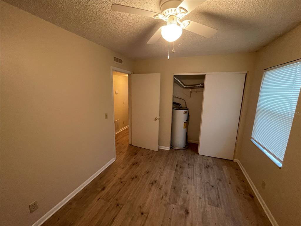 A bedroom features wood-look flooring, a ceiling fan, and a closet containing a water heater — 230 MILLARD AVENUE UNIT 1, LAKELAND, FL