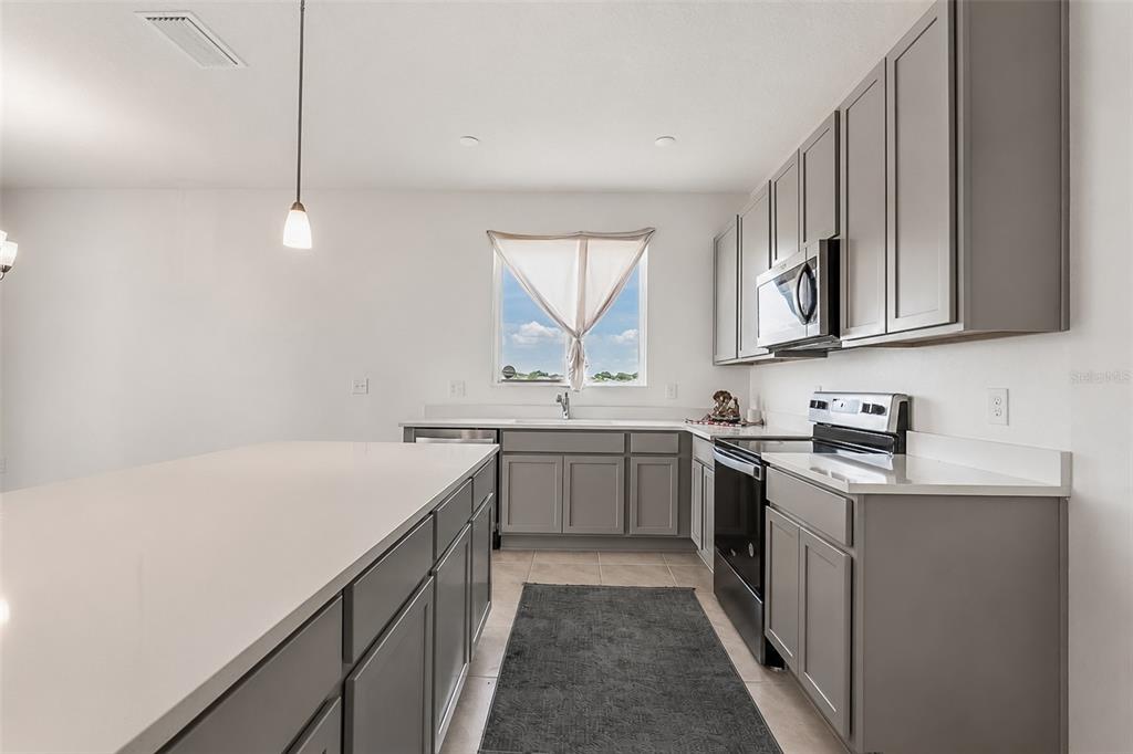A kitchen features gray cabinets, white countertops, stainless steel appliances, and a large center island — 3349 PINK OLEANDER AVENUE, MASCOTTE, FL