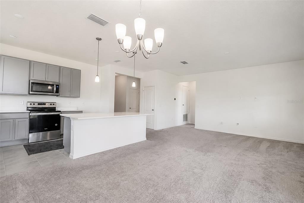 An open-concept kitchen with gray cabinets and a white island overlooks a carpeted living area — 3349 PINK OLEANDER AVENUE, MASCOTTE, FL