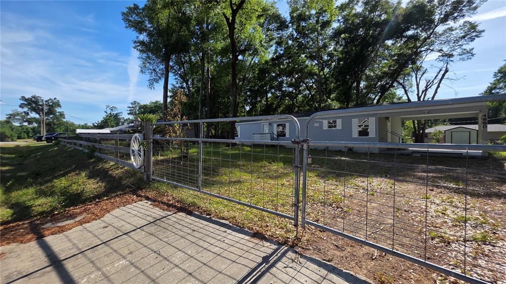 A metal gate opens to a driveway leading toward a light blue mobile home — 4880 NW 60TH TERRACE, OCALA, FL