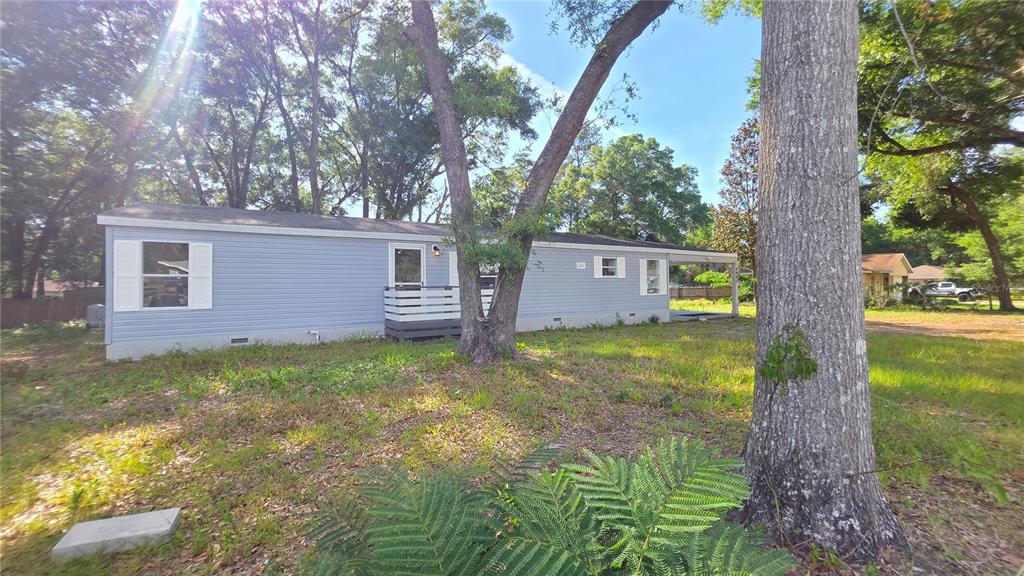 A light blue manufactured home sits on a grassy lot surrounded by large trees — 4880 NW 60TH TERRACE, OCALA, FL