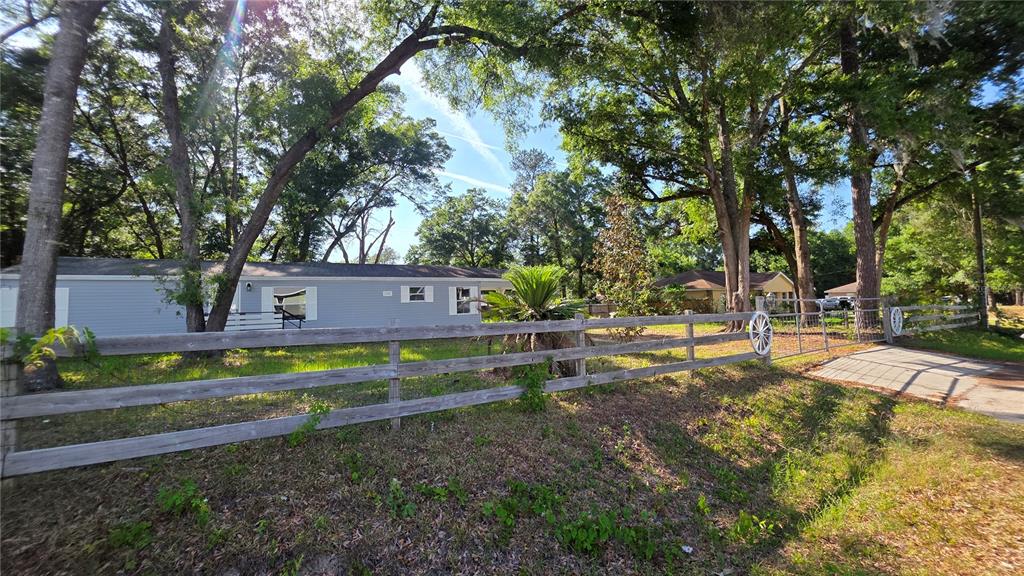 A light blue manufactured home sits behind a wooden fence on a tree-lined lot — 4880 NW 60TH TERRACE, OCALA, FL