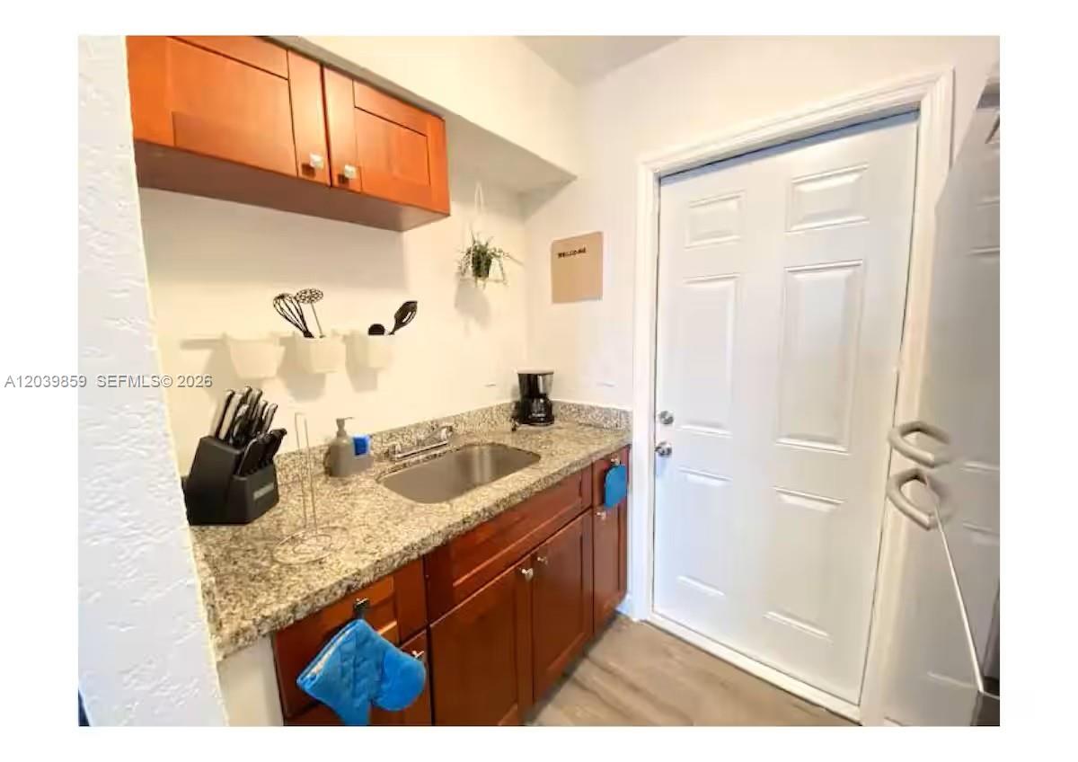 A small kitchen features wood cabinets, granite countertops, a stainless steel sink, and a door — 7638 N Miami Ave # 2, Miami FL 33150, MIAMI, FL