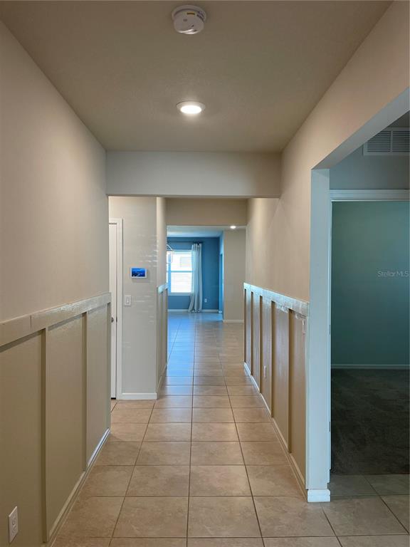 A hallway with tile flooring and wainscoting leads toward a room with a window — 5503 KEATON SPRINGS DRIVE, LAKELAND, FL