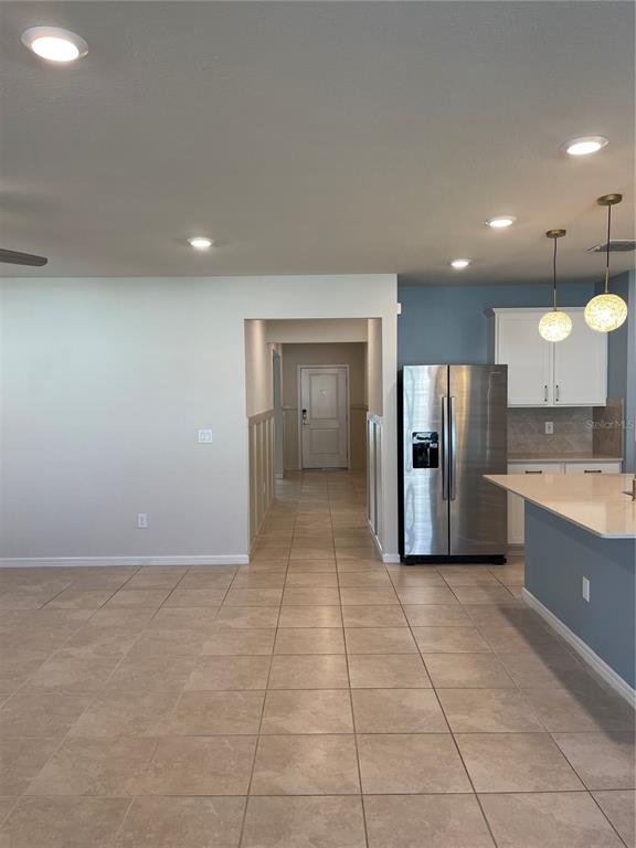 A kitchen with stainless steel appliances, white cabinets, and tile flooring opens to a hallway — 5503 KEATON SPRINGS DRIVE, LAKELAND, FL