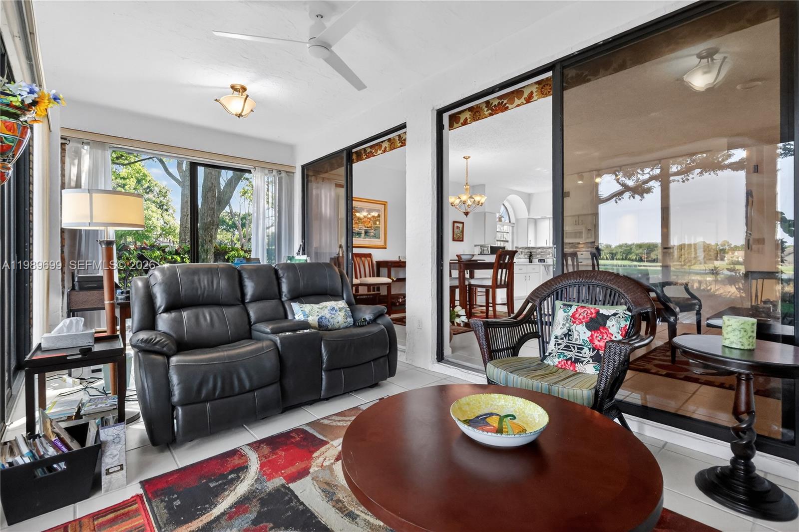 A sunroom features a black leather loveseat, wicker chair, round coffee table, and sliding glass doors — 8033 Aberdeen Dr # 102, Boynton Beach FL 33472, BOYNTON BEACH, FL