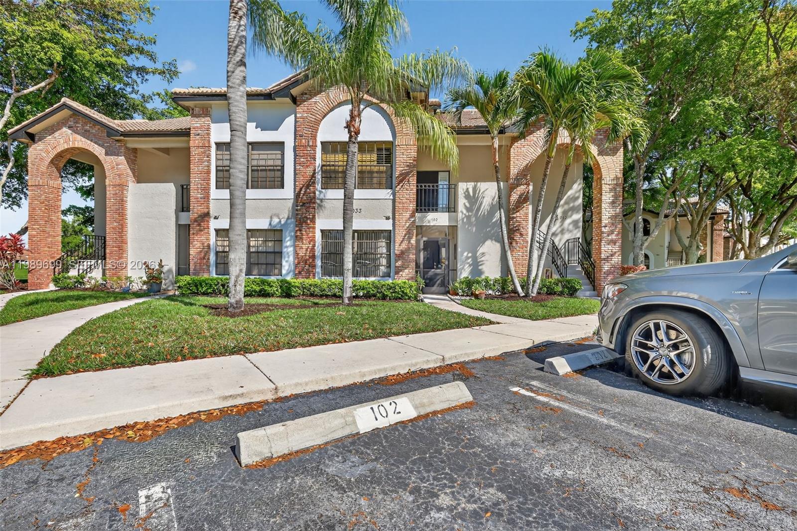 A two-story building with brick arches, palm trees, and a parking space numbered 102 — 8033 Aberdeen Dr # 102, Boynton Beach FL 33472, BOYNTON BEACH, FL