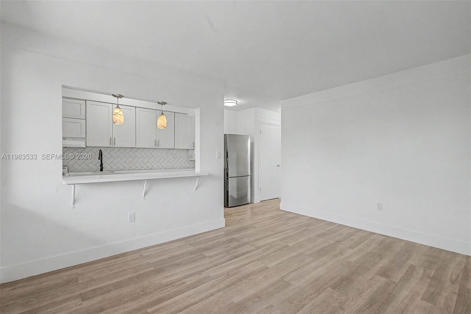A kitchen with white cabinets and a breakfast bar opens into a living area — 60 NW 79th St # 10, Miami FL 33150, MIAMI, FL