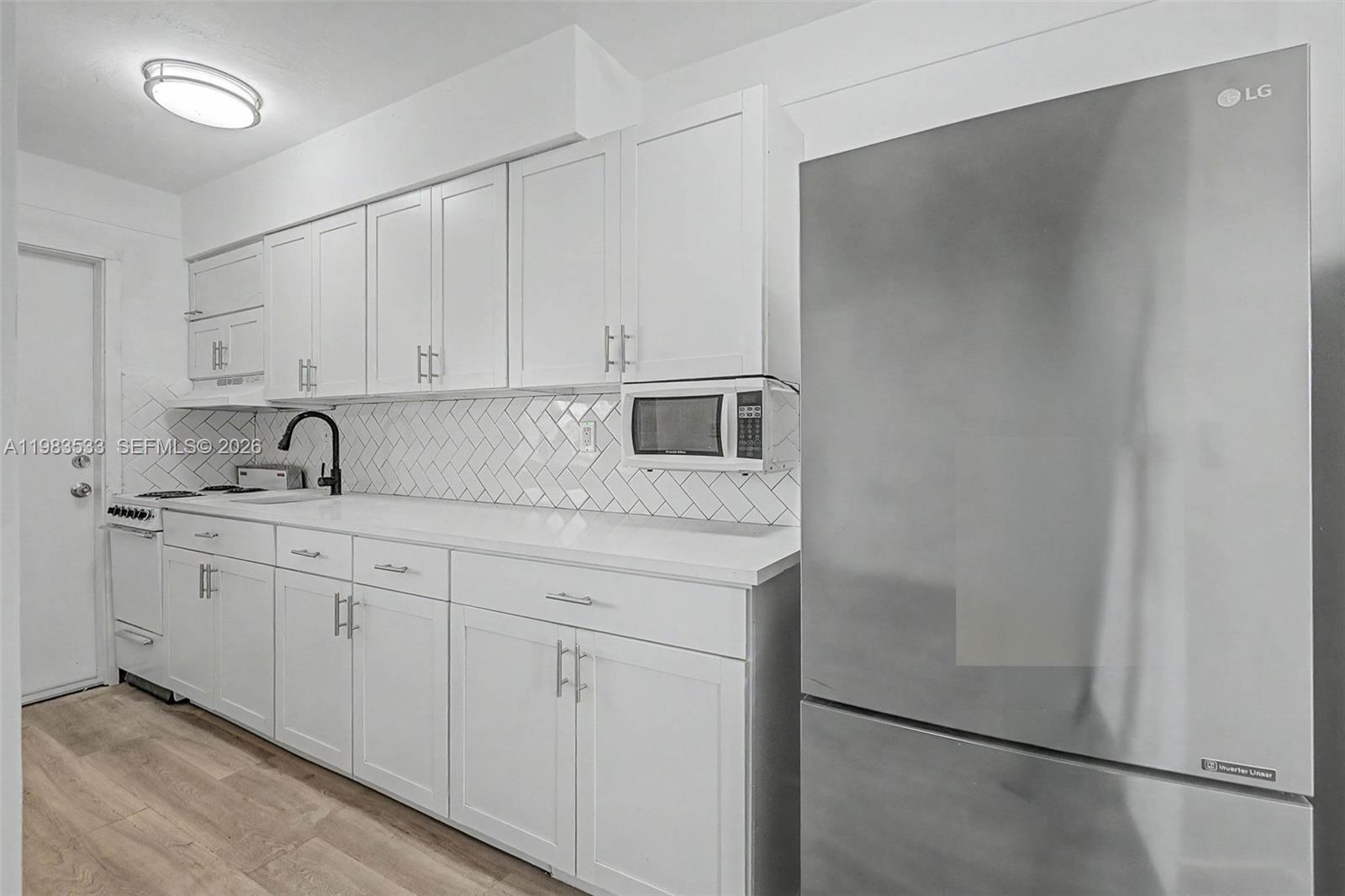 A kitchen features white cabinets, stainless steel appliances, and a herringbone-patterned tile backsplash — 60 NW 79th St # 10, Miami FL 33150, MIAMI, FL
