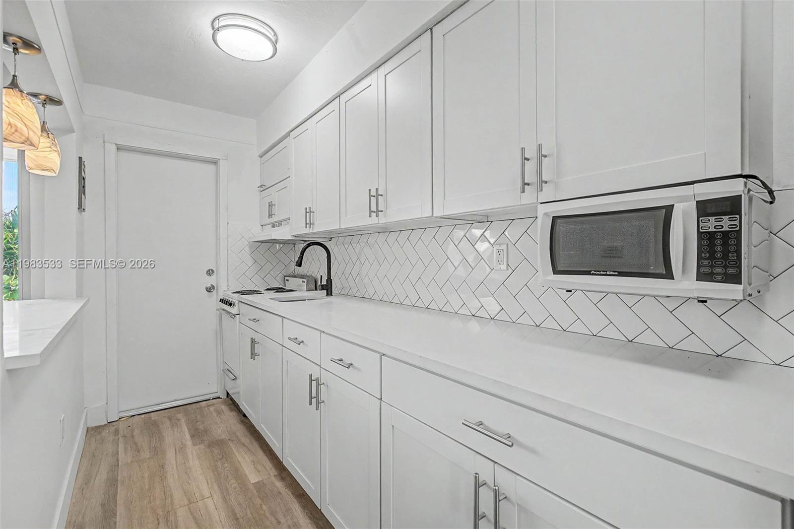 A white galley kitchen features shaker cabinets, a herringbone backsplash, and a mounted microwave — 60 NW 79th St # 10, Miami FL 33150, MIAMI, FL
