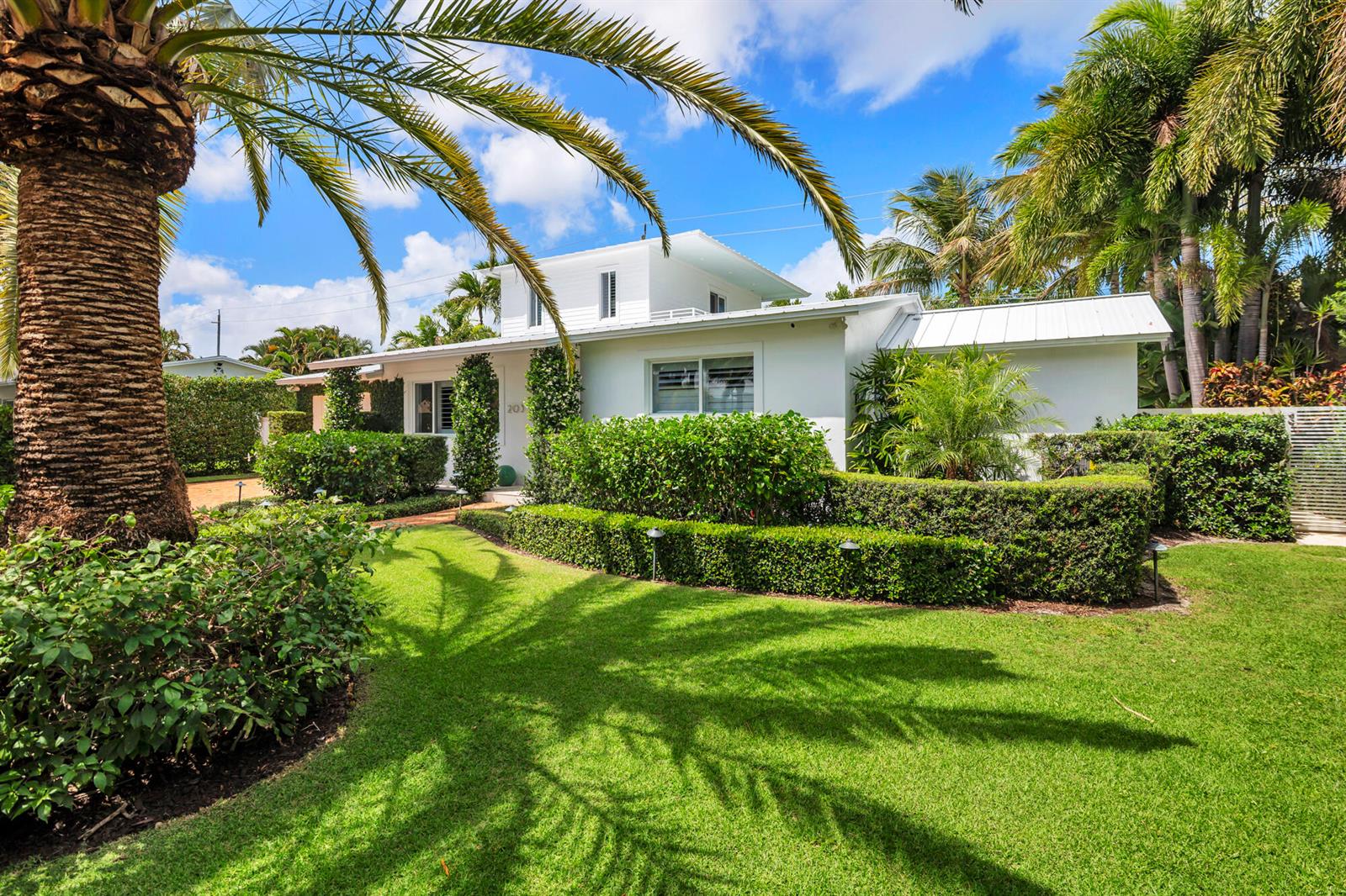 A white single-story house with a flat roof and palm trees sits behind manicured hedges — 203 Arlington Road, West Palm Beach FL 33405, WEST PALM BEACH, FL