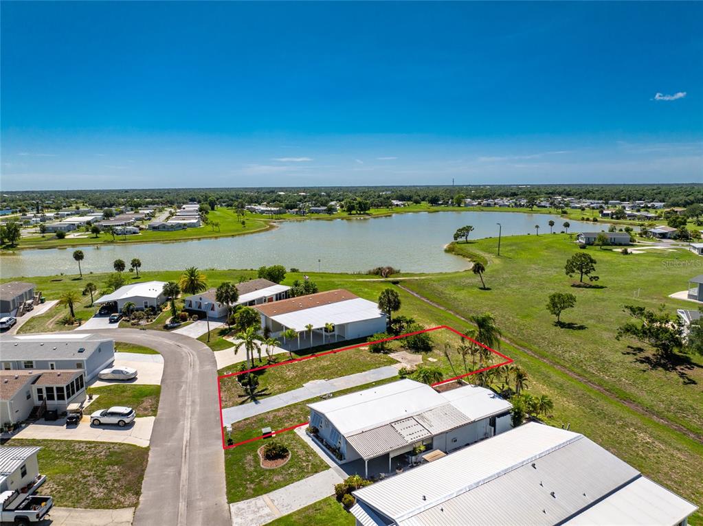 An aerial view shows a vacant residential lot outlined in red next to a lake — 7498 DANVERS CIRCLE, PORT CHARLOTTE, FL