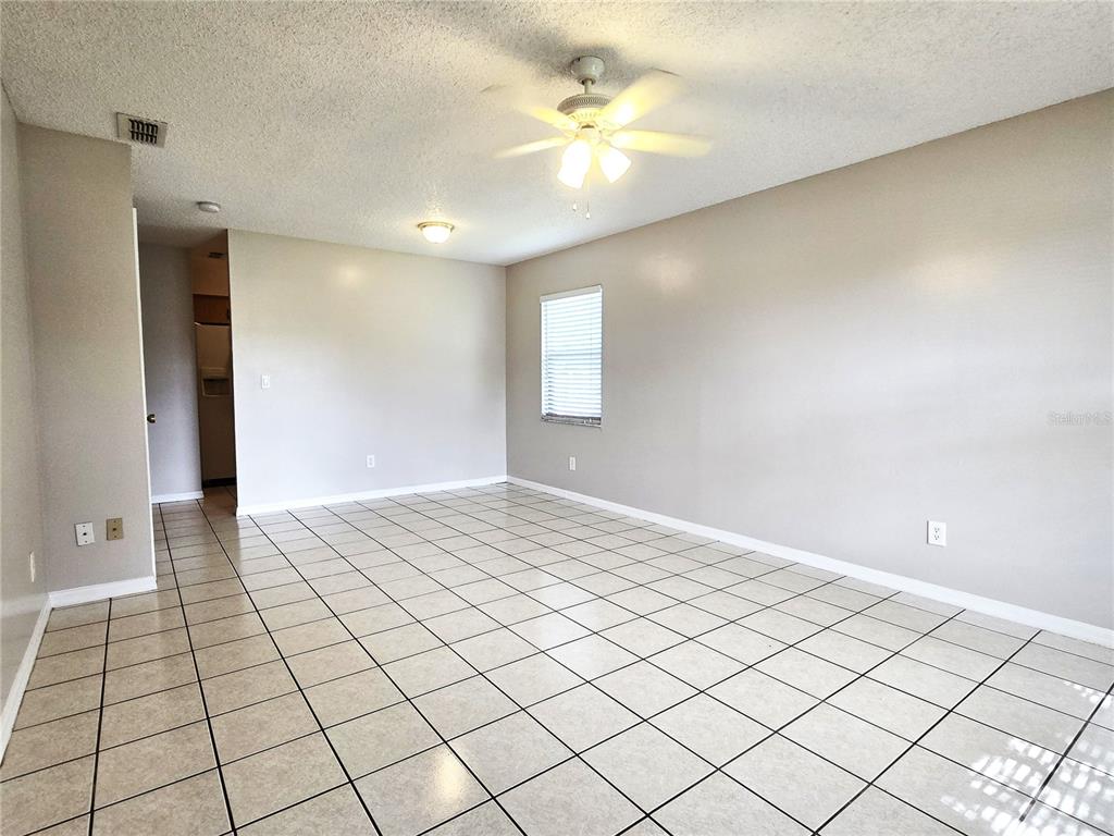 An empty room features light-colored tile flooring, beige walls, a ceiling fan, and a window — 1423 MONTANA AVENUE UNIT 1423, ST CLOUD, FL
