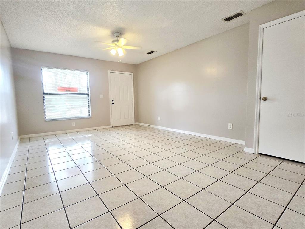 An empty room features light-colored tile flooring, beige walls, a ceiling fan, and a door — 1423 MONTANA AVENUE UNIT 1423, ST CLOUD, FL