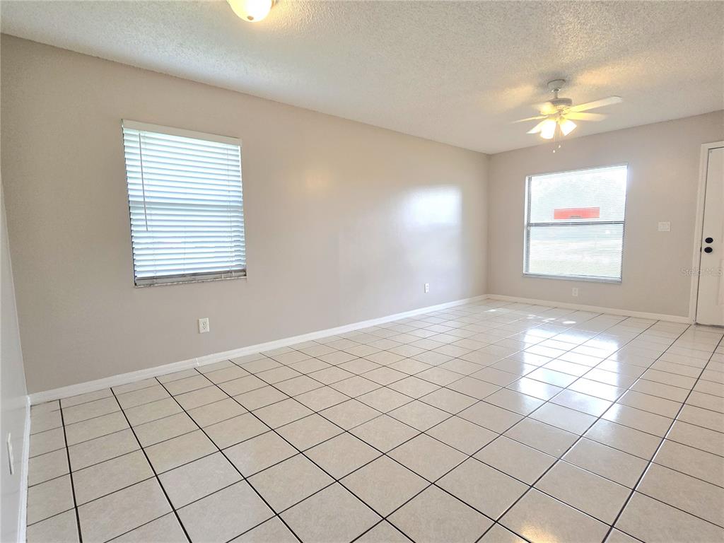 An empty room with light-colored walls, tiled flooring, two windows with blinds, and a ceiling fan — 1423 MONTANA AVENUE UNIT 1423, ST CLOUD, FL