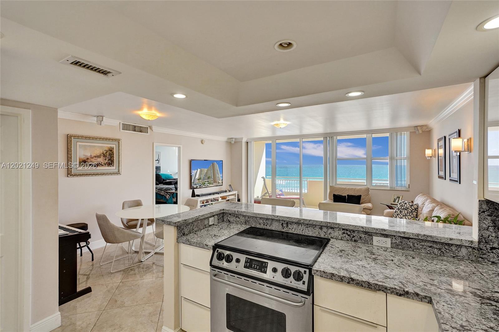 A kitchen with granite countertops overlooks a living area with ocean views through sliding doors — 3180 S Ocean Dr # 415, Hallandale Beach FL 33009, HALLANDALE BEACH, FL
