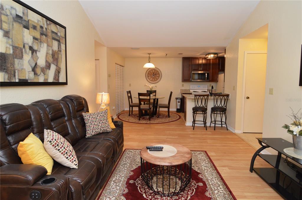 An open-concept living and dining area features a leather sofa, wood flooring, and kitchen island — 10263 GANDY BOULEVARD N UNIT 602, ST PETERSBURG, FL