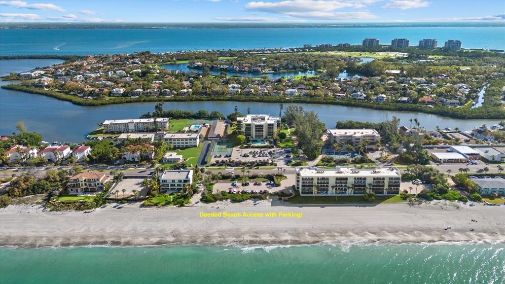 An aerial view shows beachfront condominiums, a parking lot, and a waterway near the coast — 3240 GULF OF MEXICO DRIVE UNIT B402, LONGBOAT KEY, FL