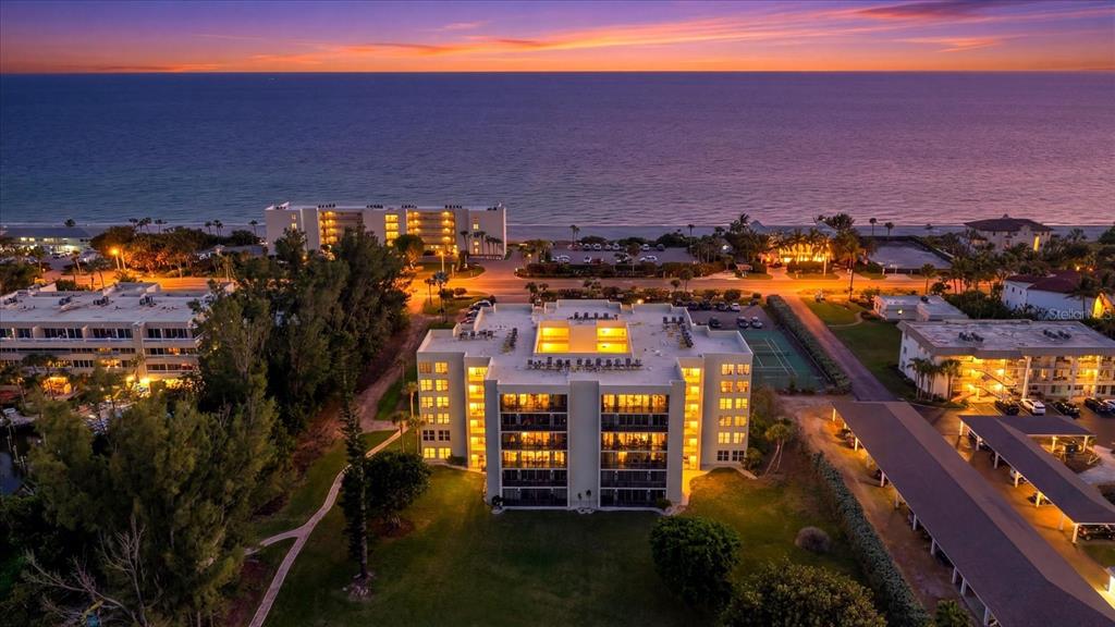 An aerial view of a multi-story apartment building near the ocean at sunset — 3240 GULF OF MEXICO DRIVE UNIT B402, LONGBOAT KEY, FL